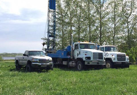 Photo of our well drilling rigs in a field with some trees and a body of water in the background.